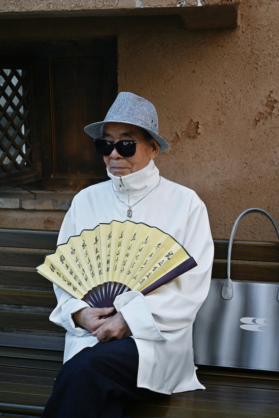 a man sitting on a bench holding a fan