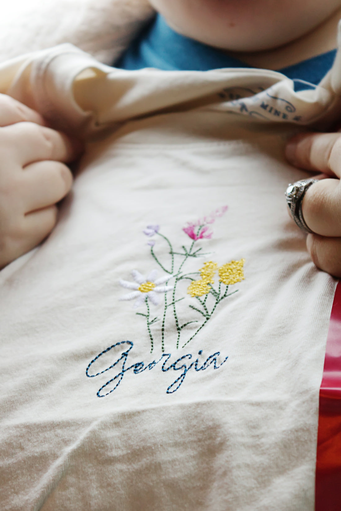A baby is holding onto a t - shirt with flowers on it