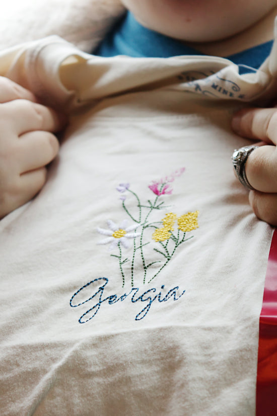 A baby is holding onto a t - shirt with flowers on it