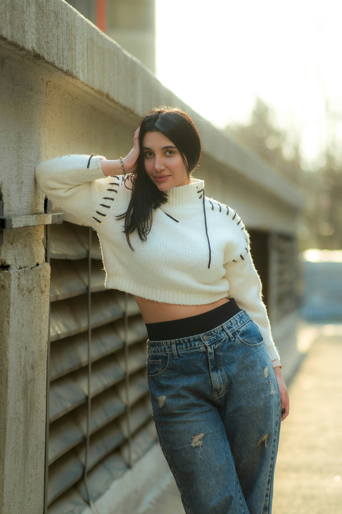 Young woman in white sweater and jeans leans on wall