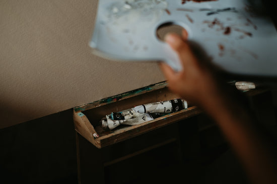 Artist's hand holding palette over paint tubes