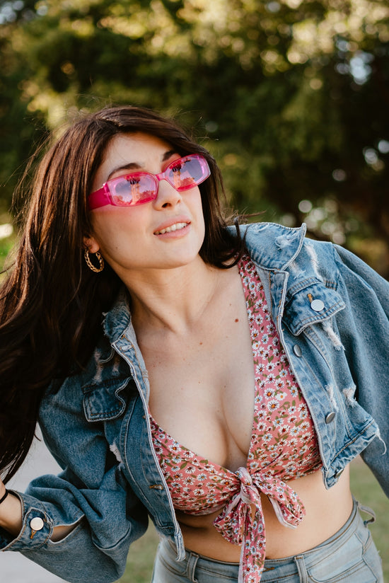 Woman in denim jacket and floral top wearing pink sunglasses