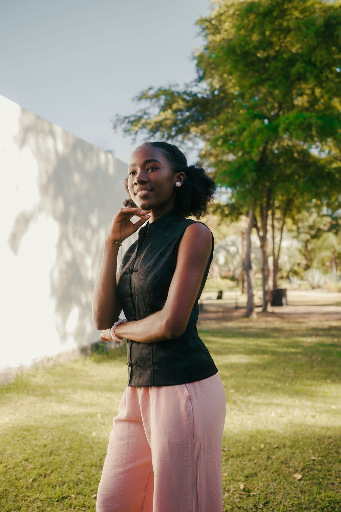 Young woman in black top and pink pants outdoors.