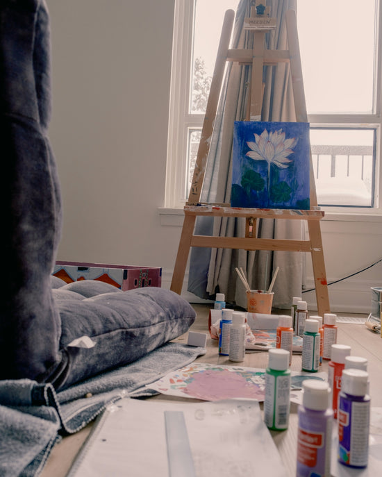 An easel displays a painting of a white lotus flower.