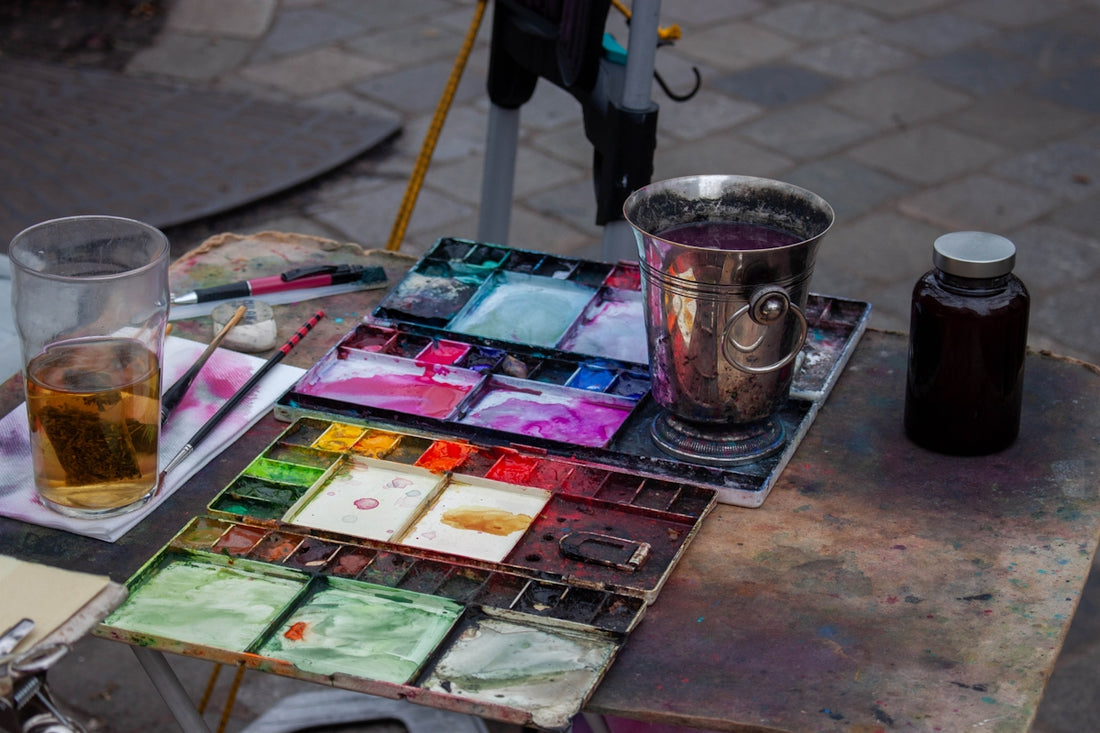 Watercolor paints, brushes, and drinks on a table.