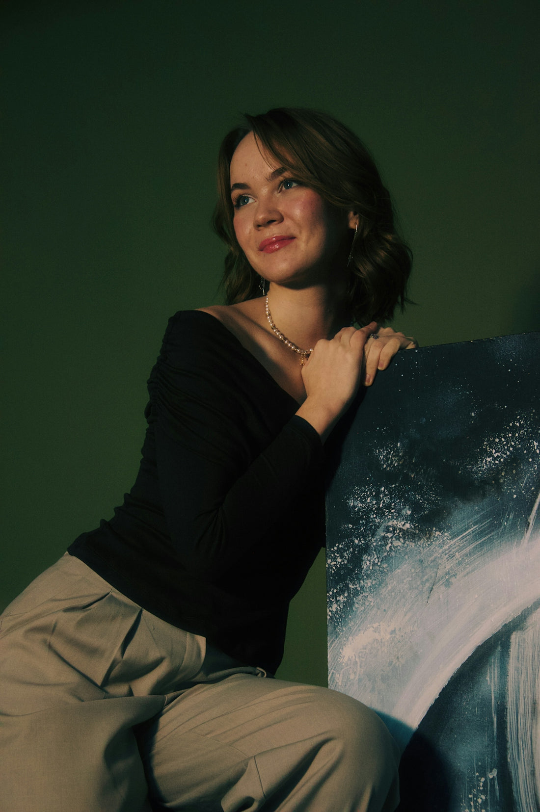 A young woman leans on abstract art against green background