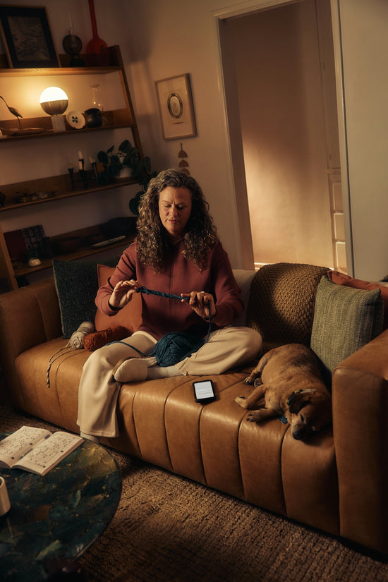 Woman knitting on couch with dog sleeping nearby