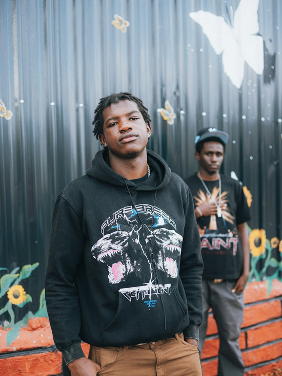Two young men stand in front of a mural